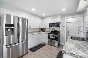 Kitchen with stainless steel appliances, decorative backsplash, light wood-type flooring, white cabinetry, and recessed lighting