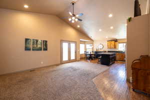 Carpeted living area with recessed lighting, healthy amount of natural light, high vaulted ceiling, a ceiling fan, and wood finished floors