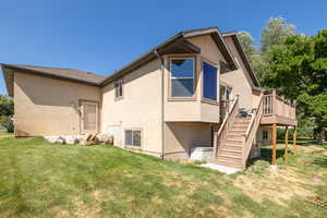 Rear view of house with stairs, stucco siding, a wooden deck, and a lawn