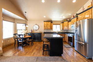 Kitchen with stainless steel appliances, a breakfast bar, wood finished floors, recessed lighting, and vaulted ceiling