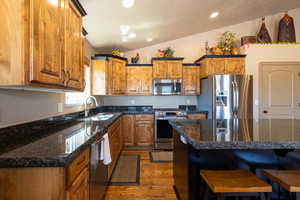 Kitchen featuring appliances with stainless steel finishes, vaulted ceiling, dark wood-type flooring, brown cabinets, and a breakfast bar
