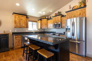 Kitchen featuring appliances with stainless steel finishes, dark wood-type flooring, recessed lighting, a kitchen breakfast bar, and vaulted ceiling