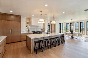 Kitchen with light wood-style floors, recessed lighting, a breakfast bar, a large island with sink, and tasteful backsplash