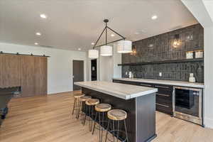 Community bar area with beverage cooler, light wood-type flooring, decorative backsplash, recessed lighting, and a barn door