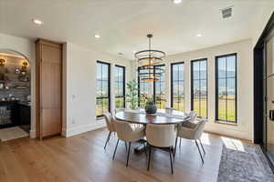 Dining area with healthy amount of natural light, light wood-type flooring, a chandelier, recessed lighting, and wine cooler