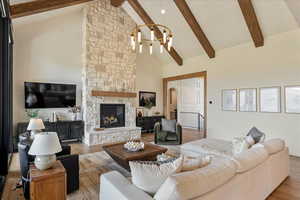 Living area with high vaulted ceiling, a chandelier, beam ceiling, light wood-type flooring, and a stone fireplace
