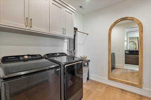 Laundry room with cabinet space, washer and clothes dryer, light wood finished floors, and arched walkways