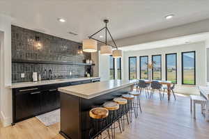 Indoor wet bar with backsplash, light wood finished floors, recessed lighting, and hanging light fixtures