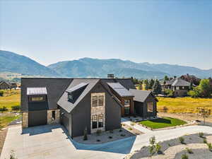 View of front of property featuring stone siding, driveway, a chimney, a mountain view, and roof with shingles