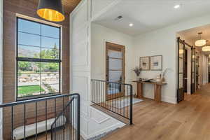 Hallway featuring a barn door, light wood-style flooring, an upstairs landing, and recessed lighting
