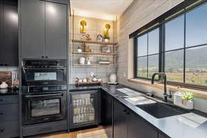 Kitchen with black appliances, wine cooler, tasteful backsplash, dark countertops, and open shelves