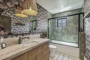 Bathroom with wallpapered walls, vanity, tile patterned flooring, and bath / shower combo with glass door