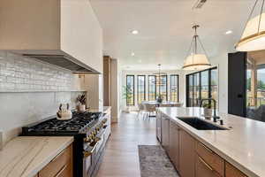 Kitchen with stainless steel gas range oven, recessed lighting, light stone counters, tasteful backsplash, and wall chimney exhaust hood