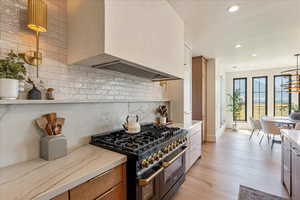 Kitchen with double oven range, recessed lighting, decorative backsplash, light wood-style floors, and custom range hood