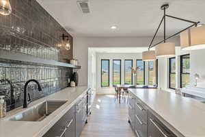 Kitchen featuring light wood finished floors, recessed lighting, backsplash, gray cabinets, and hanging light fixtures