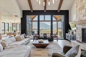 Living area featuring wood finished floors, a chandelier, beamed ceiling, and a stone fireplace