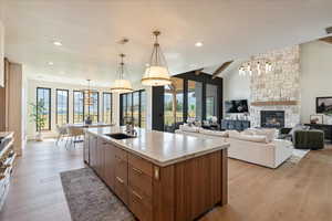 Kitchen with a chandelier, a large island with sink, light wood finished floors, brown cabinetry, and recessed lighting