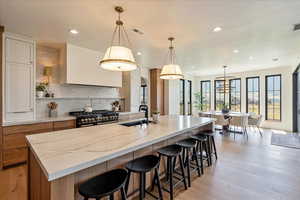 Kitchen with recessed lighting, decorative backsplash, a large island, light stone countertops, and ventilation hood