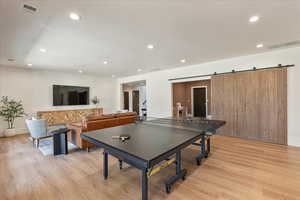 Rec room with light wood-style flooring, a barn door, and recessed lighting