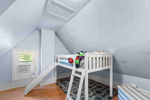 Bedroom featuring attic access, wood finished floors, and vaulted ceiling