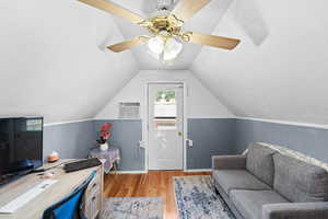 Office space featuring light wood-style floors, a ceiling fan, vaulted ceiling, an AC wall unit, and a wainscoted wall