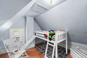 Bedroom featuring attic access, vaulted ceiling, and wood finished floors