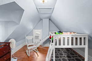 Bedroom with wood finished floors, lofted ceiling, and attic access