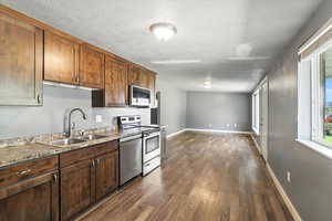 Kitchen with dark wood finished floors, stainless steel appliances, and a textured ceiling