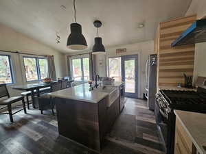 Kitchen featuring appliances with stainless steel finishes, dark wood finished floors, vaulted ceiling, a kitchen island with sink, and pendant lighting