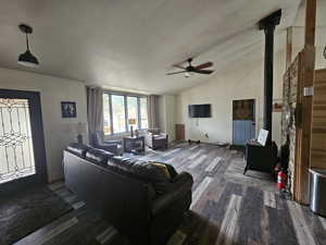 Living room featuring lofted ceiling, dark wood-style flooring, a ceiling fan, and a wood stove