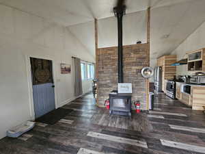 Living room featuring a wood stove, high vaulted ceiling, and dark wood-type flooring