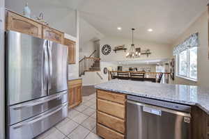 Kitchen featuring appliances with stainless steel finishes, vaulted ceiling, light tile patterned flooring, a chandelier, and decorative light fixtures