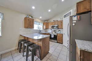 Kitchen with a peninsula, stainless steel appliances, decorative backsplash, a kitchen bar, and recessed lighting