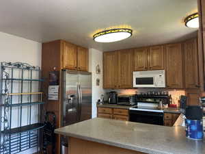 Kitchen featuring black electric range oven, a peninsula, white microwave, and brown cabinets
