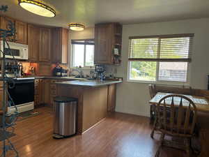 Kitchen featuring a peninsula, light wood-type flooring, white appliances, brown cabinetry, and open shelves