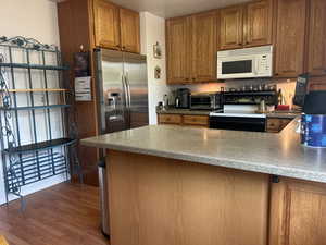 Kitchen with black / electric stove, brown cabinets, white microwave, wood finished floors, and a peninsula