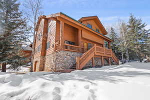 View of front of home with stone siding, a porch, and stairs