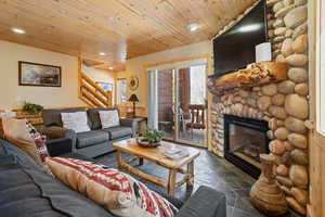 Living area featuring stone tile flooring, recessed lighting, stairway, wood ceiling, and a stone fireplace