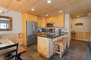 Kitchen featuring light brown cabinetry, a wainscoted wall, stainless steel appliances, a kitchen breakfast bar, and wooden ceiling