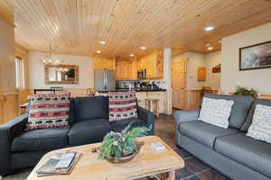 Living room with stone tile floors, wood ceiling, a wainscoted wall, recessed lighting, and a chandelier