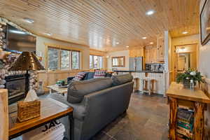 Living area with recessed lighting, dark stone finish floors, wooden ceiling, a stone fireplace, and a chandelier
