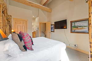Carpeted bedroom with beam ceiling, a high ceiling, connected bathroom, and recessed lighting