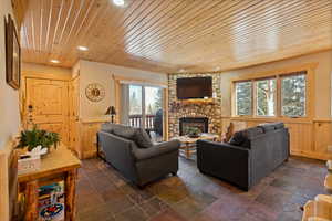 Living area with healthy amount of natural light, wood ceiling, wainscoting, a stone fireplace, and recessed lighting