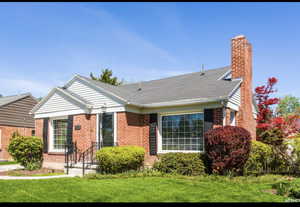 View of front of house featuring a chimney, a front lawn, brick siding, and roof with shingles