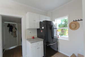 Kitchen featuring freestanding refrigerator, light wood-type flooring, white cabinets, light countertops, and crown molding