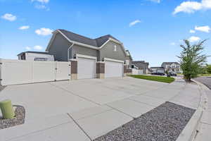 View of side of property with a gate, an attached garage, stucco siding, driveway, brick siding, and three car garage