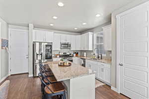 Kitchen featuring appliances with stainless steel finishes, a kitchen island, dark wood-style flooring, granite countertops, and recessed lighting