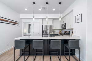 Kitchen with a peninsula, light countertops, white cabinetry, appliances with stainless steel finishes, and a kitchen breakfast bar