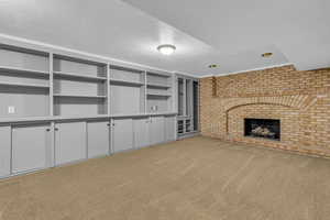 Unfurnished living room featuring light colored carpet, a brick fireplace, brick wall, and a textured ceiling