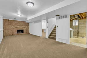 Unfurnished living room featuring carpet flooring, stairway, and a brick fireplace